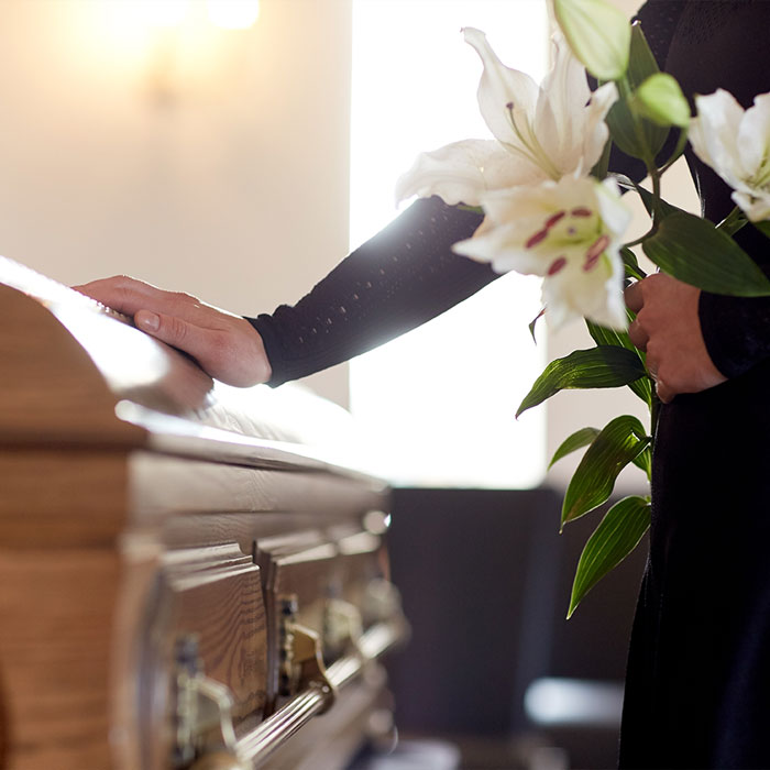 Pompes funèbres LOIC - Photo d'un cercueil et une main de femme posée, l'autre tenant un bouquet lors d'obsèques