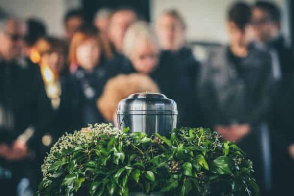Urne en métal avec les cendres d'une personne décédée lors d'une cérémonie, avec des personnes en deuil en arrière-plan lors d'un service commémoratif. Dernier adieu à une personne dans une urne.